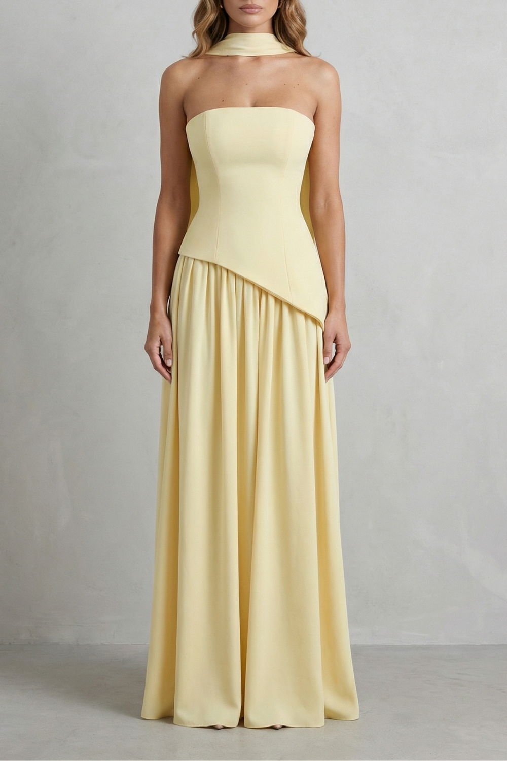 Front view of a pale yellow strapless asymmetric maxi dress featuring a structured bodice and a gathered skirt.