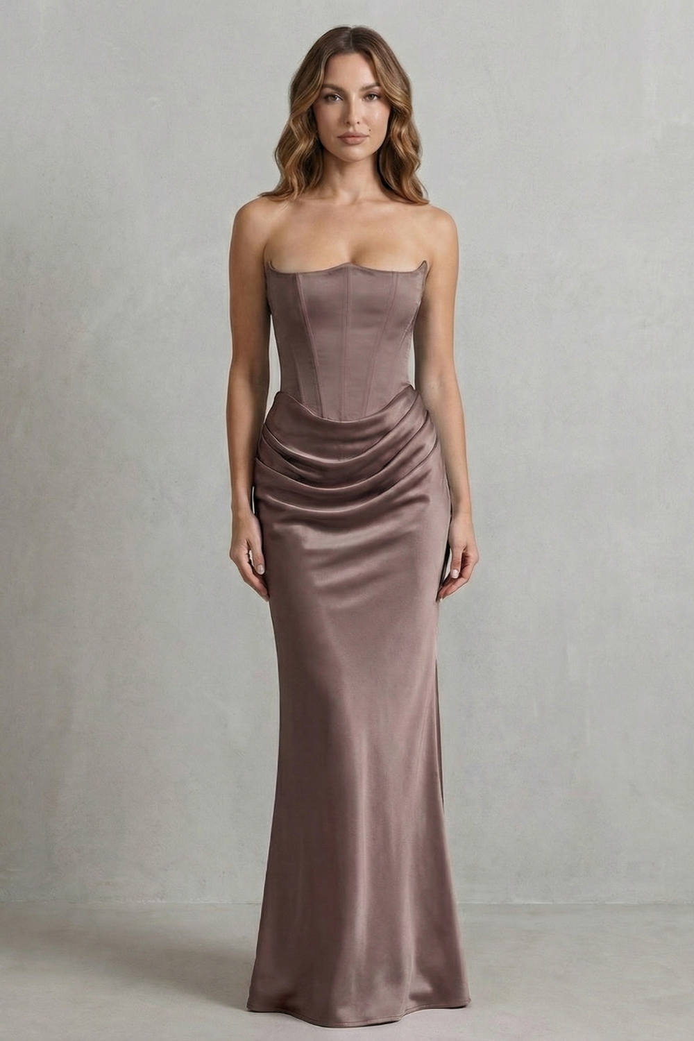 Front view of a woman in a sophisticated brown-taupe satin dress, featuring a strapless corset and draped maxi skirt.