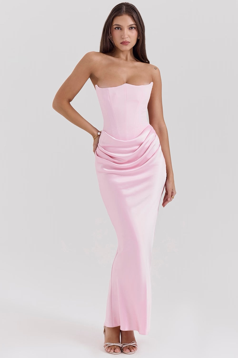 Full body shot of a woman wearing a light pink strapless corset maxi dress with a draped ruched waist.