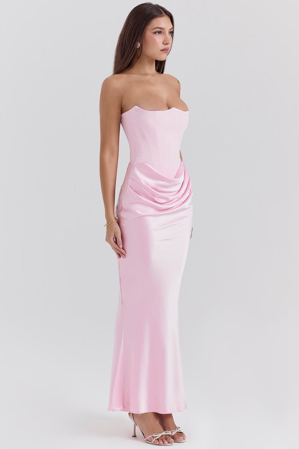 Side profile of a woman in a light pink strapless corset maxi dress, highlighting the fitted silhouette and ruched detail.