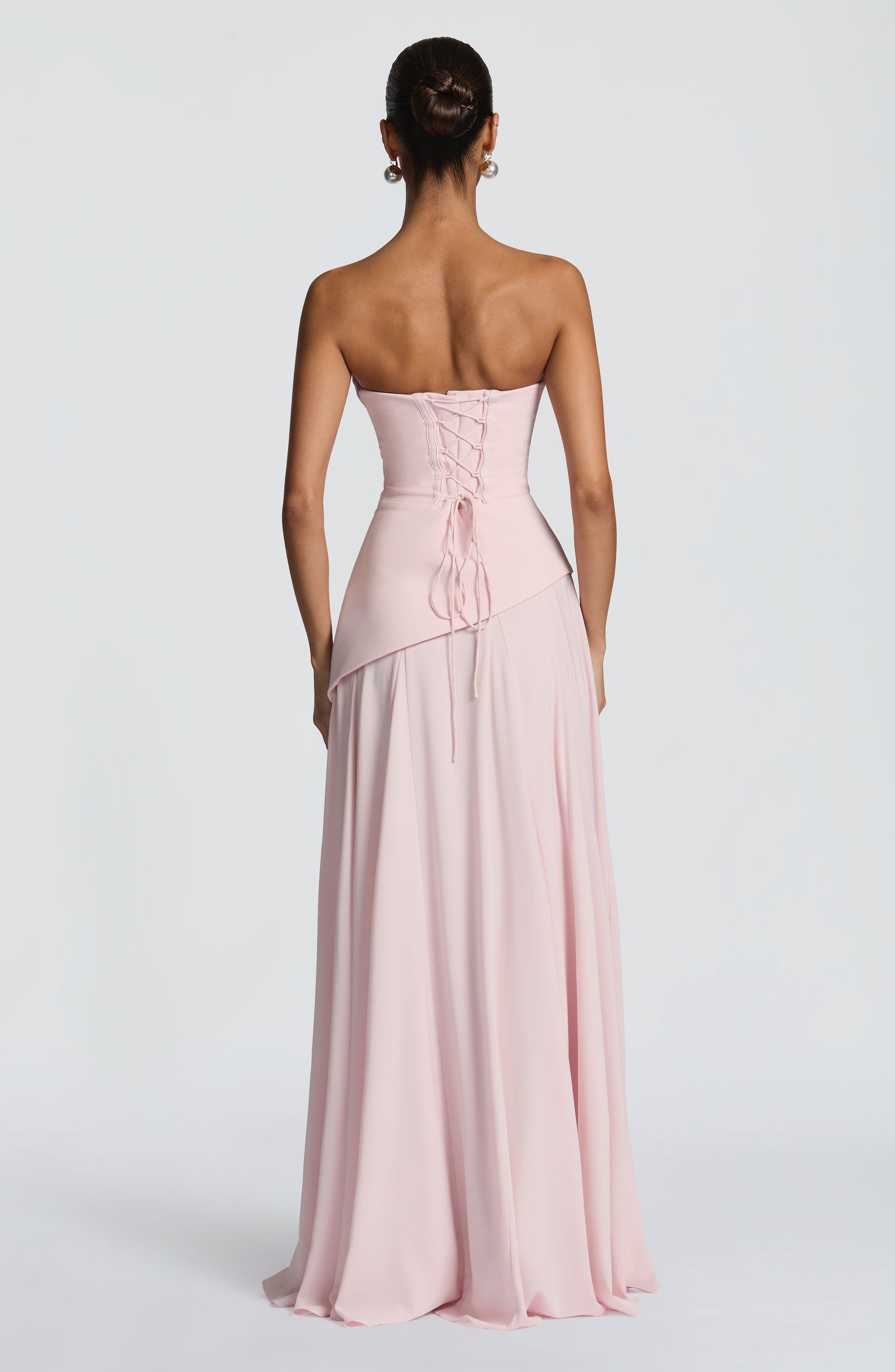 Back view of a light pink strapless cowl neck maxi dress with a lace-up corset back and flowing skirt.