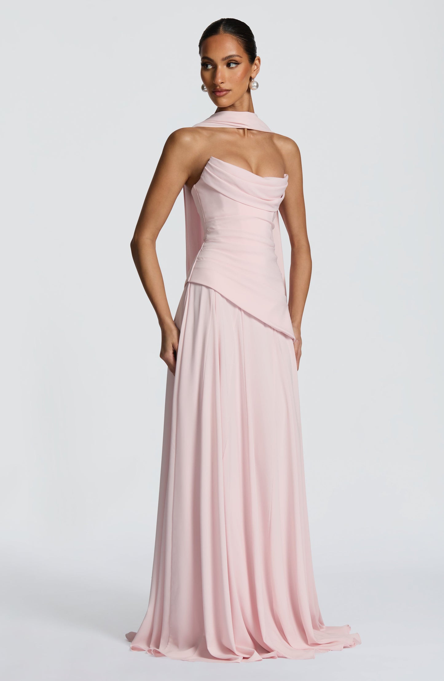 Front view of a light pink strapless cowl neck maxi dress with a long scarf detail draped over the shoulder.