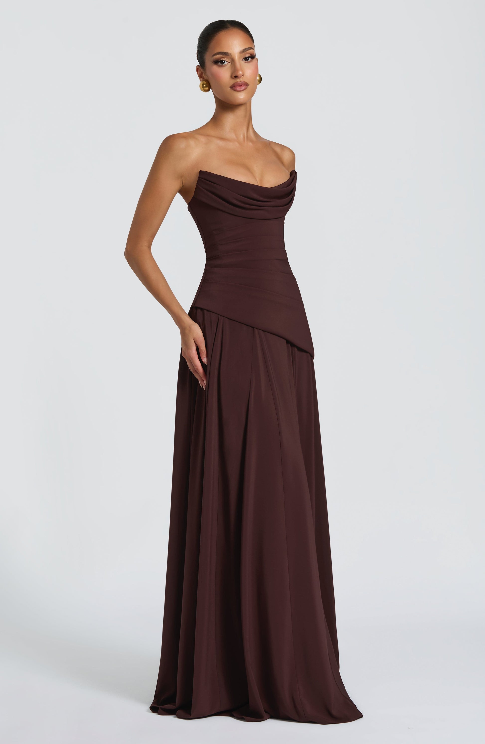 Side view of a dark brown strapless cowl neck maxi dress, showcasing the draped neckline and full skirt.