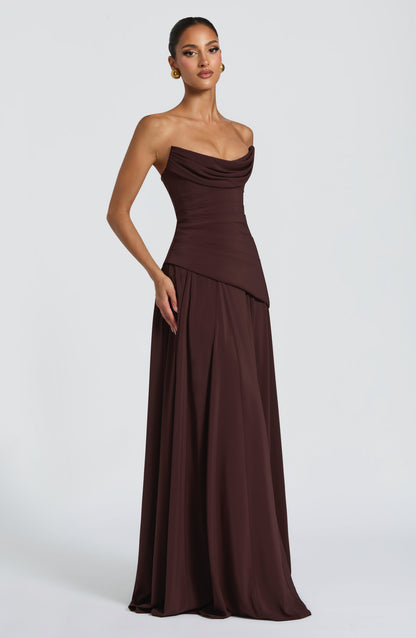Side view of a dark brown strapless cowl neck maxi dress, showcasing the draped neckline and full skirt.