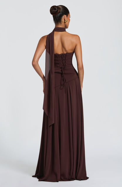 Back view of a dark brown strapless cowl neck maxi dress, featuring a lace-up corset and flowing scarf.