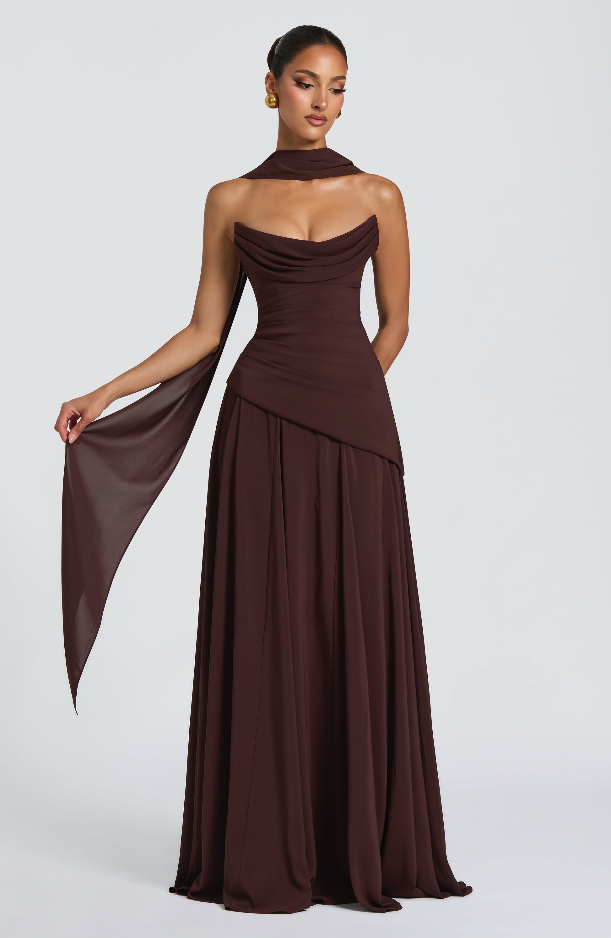 Rich brown strapless cowl neck maxi dress with a draped bodice and a full, flowing skirt, perfect for an evening dress.
