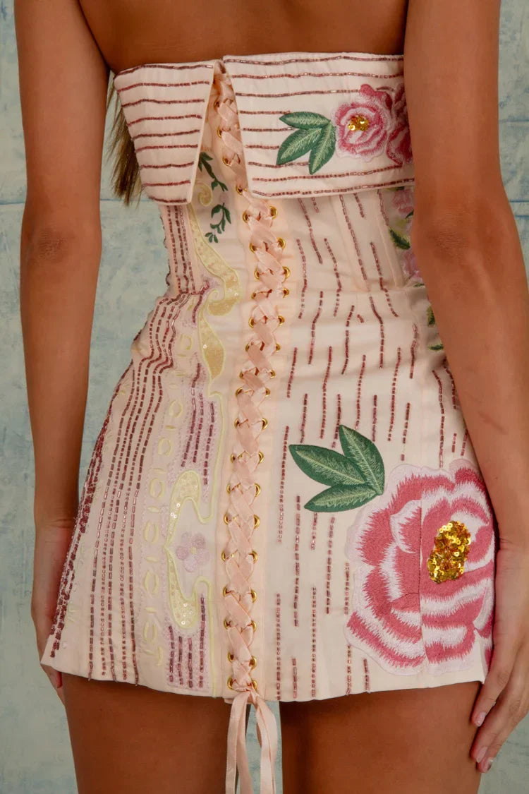 Close-up of the back corset detail on the strapless mini dress, with pink ribbon lacing and floral embroidery.
