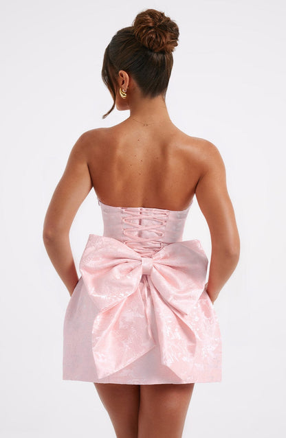 Back view of a light pink strapless floral mini dress, highlighting the corset-style lace-up closure and large bow.
