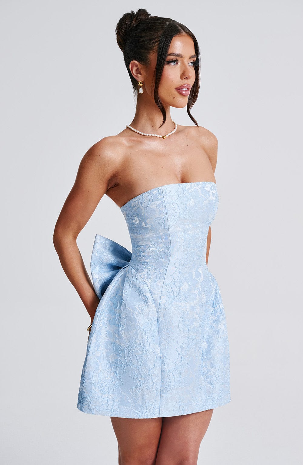 Side profile of a women's light blue strapless floral bow mini dress, showing the subtle bow at the back.