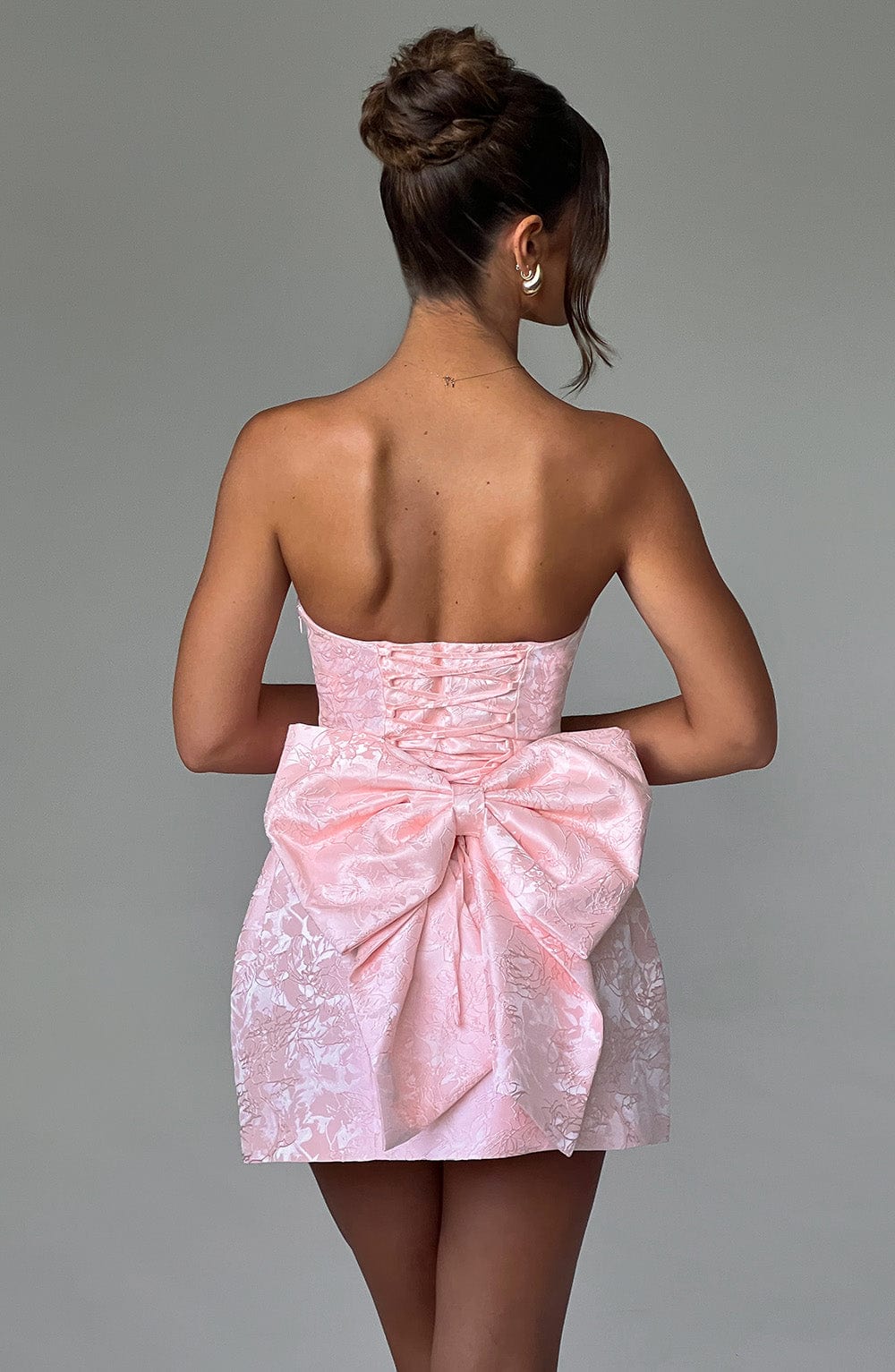 Back view of the light pink strapless floral mini dress, showcasing a large bow detail and corset-style lacing.