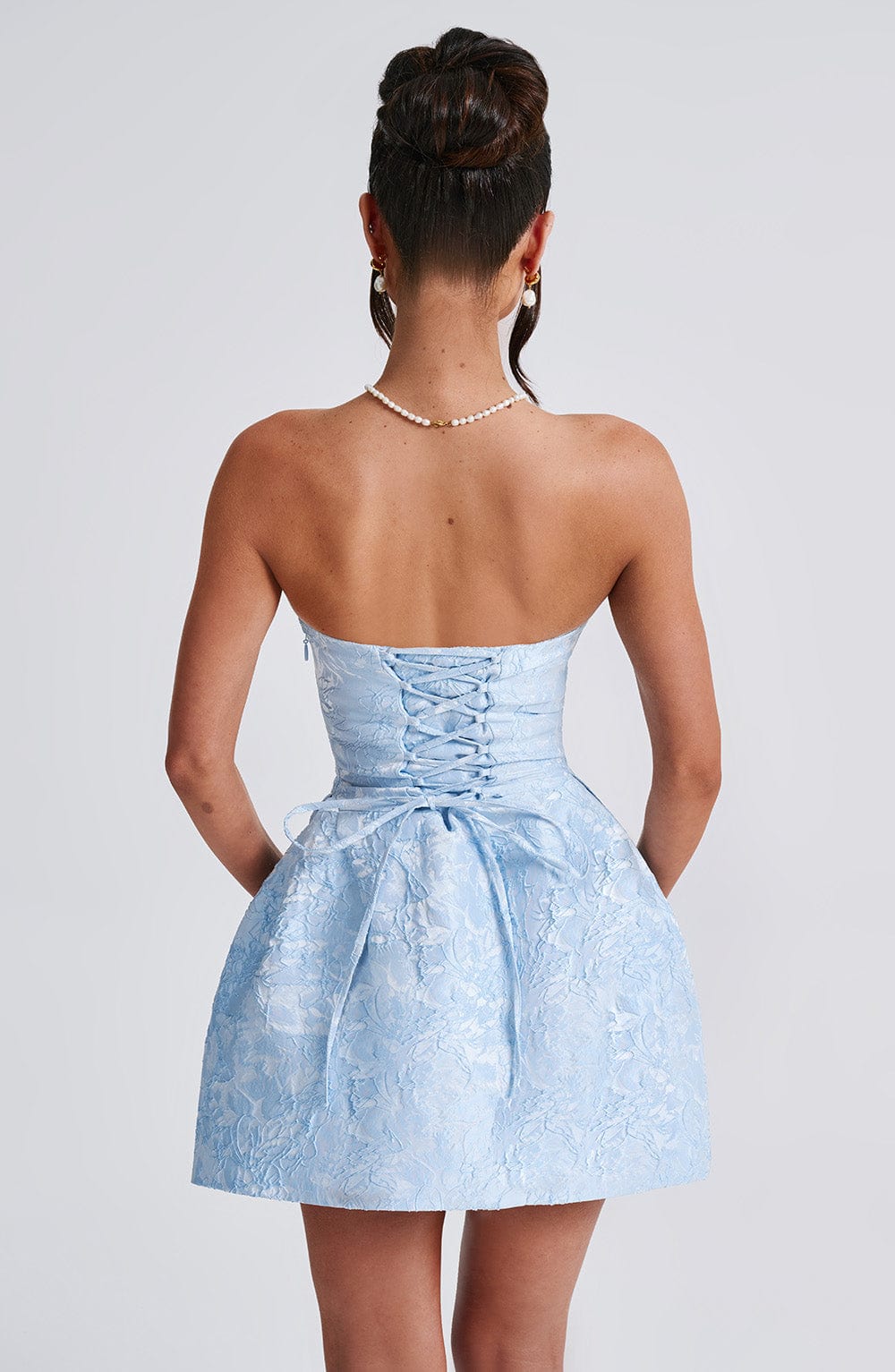 Back view of a women's light blue strapless floral mini dress, featuring the lace-up corset and small back bow.