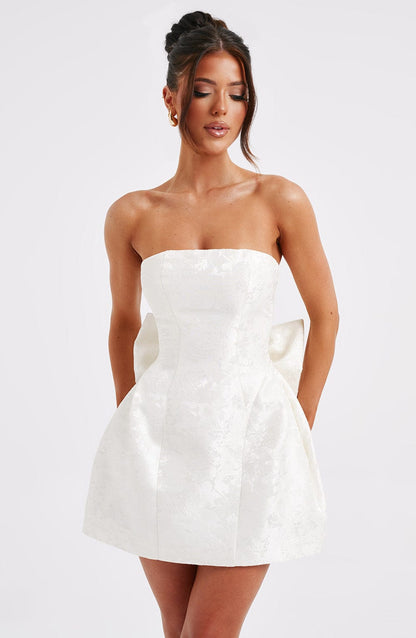 Front view of a women's white strapless mini dress with subtle floral texture and a large bow.