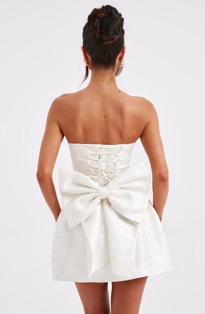 Rear view of a white strapless mini dress featuring a large bow and delicate corset back lacing.