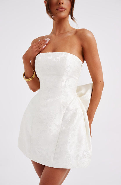 Close-up of a white strapless mini dress with a subtle floral pattern, showing the side bow detail.