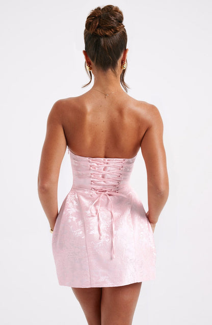 Direct back view of the women's light pink strapless floral mini dress, emphasizing the lace-up corset and subtle floral pattern.
