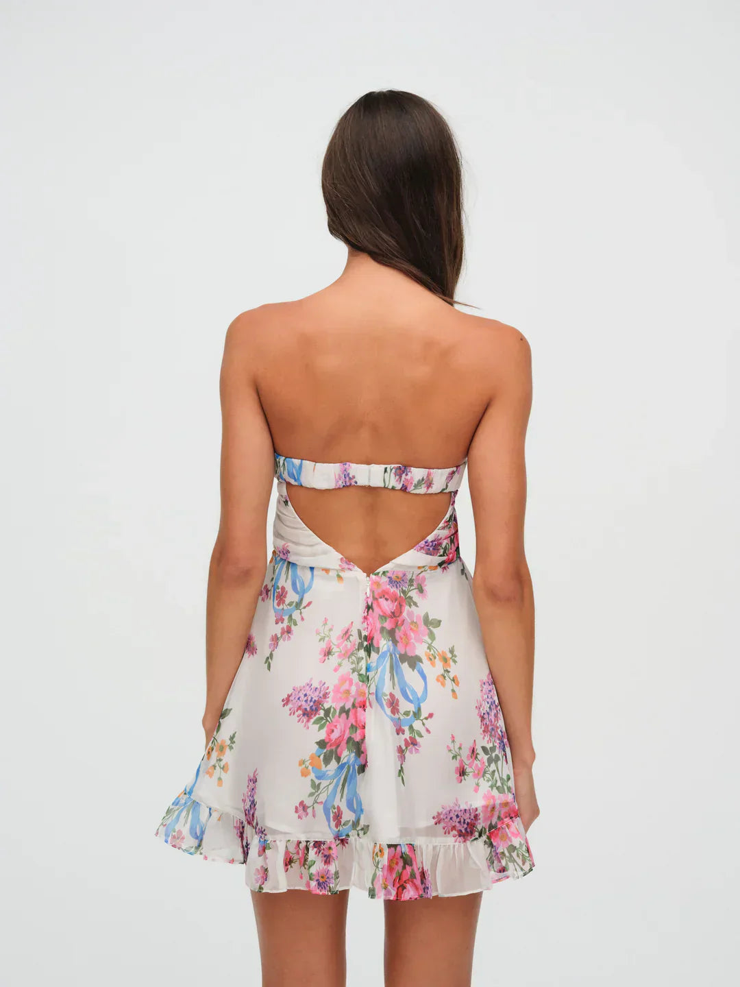 Back view of a women's strapless floral mini dress with an open-back design, showcasing the white fabric with pink and purple flowers and a ruffled hem.