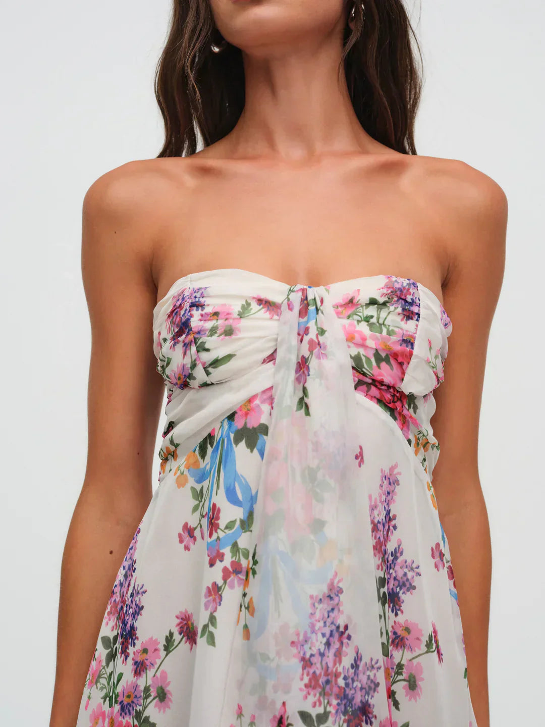 Close-up of the bust and torso of a women's strapless floral mini dress, highlighting the knotted detail and the vibrant pink, purple, and blue floral pattern.