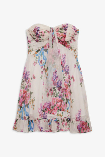 Flat lay of a white strapless floral mini dress with pink, purple, and blue flowers, featuring a knotted front and a delicate ruffled hem, ideal for vacation dresses.