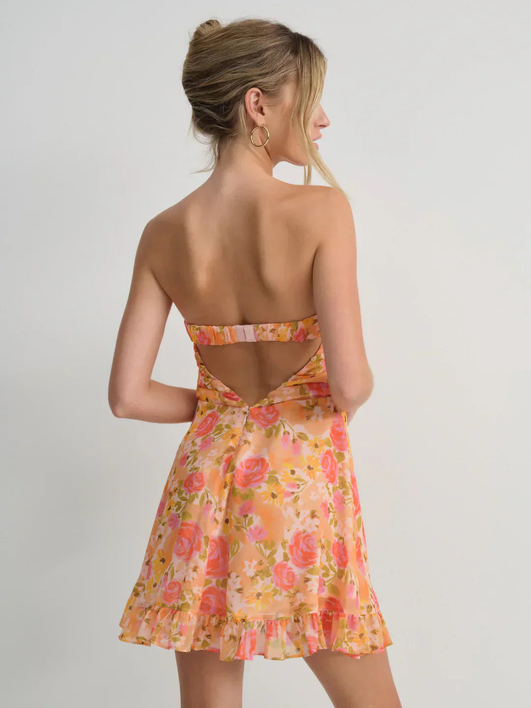 Back view of a women's strapless mini dress in a vibrant orange and pink floral print, showcasing the open-back design and ruffled hem.