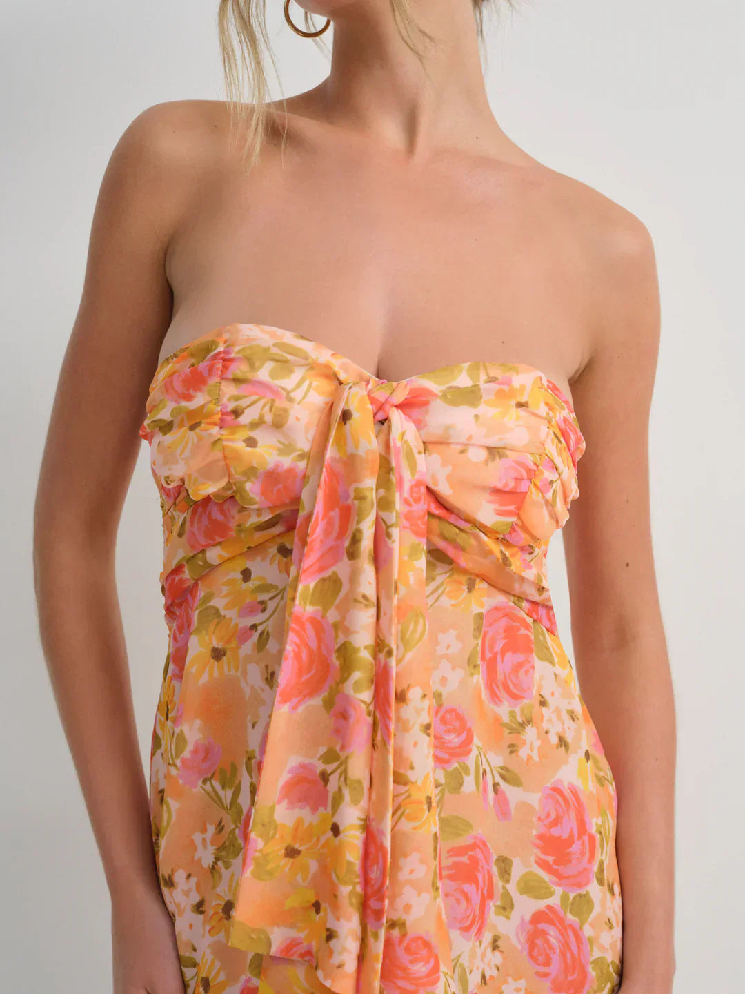 Close-up of the bust of an orange and pink floral strapless mini dress, highlighting the knotted detail and the warm-toned flower pattern.