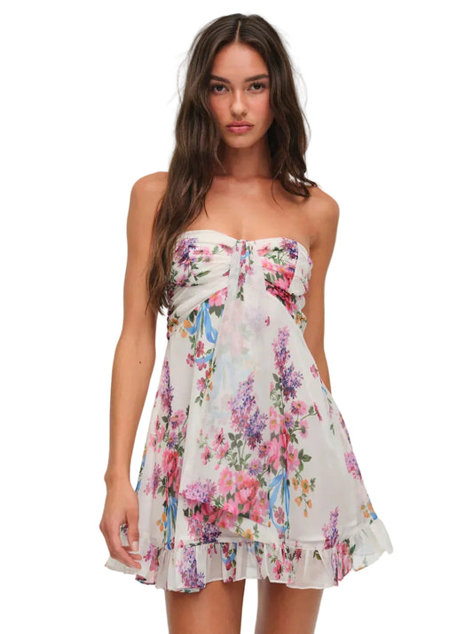 Front view of a women's strapless mini dress in white with vibrant pink, purple, and blue floral print, featuring a ruffled hem and a knotted bust detail.