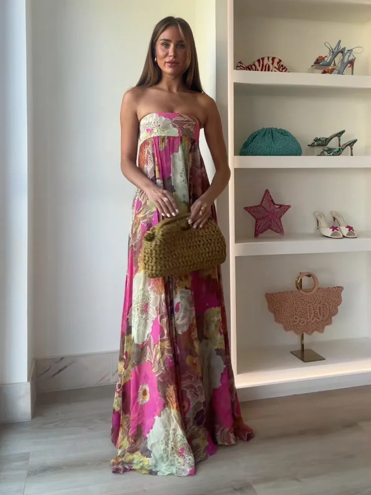 Front view of a women's strapless floral printed maxi dress, showcasing the full length and vibrant pattern, styled with a small woven clutch.