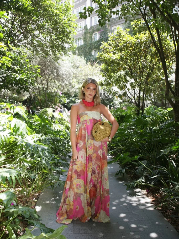 Women's strapless floral printed maxi dress in a garden setting, showcasing the full length and bright floral pattern, suitable for vacation dresses.