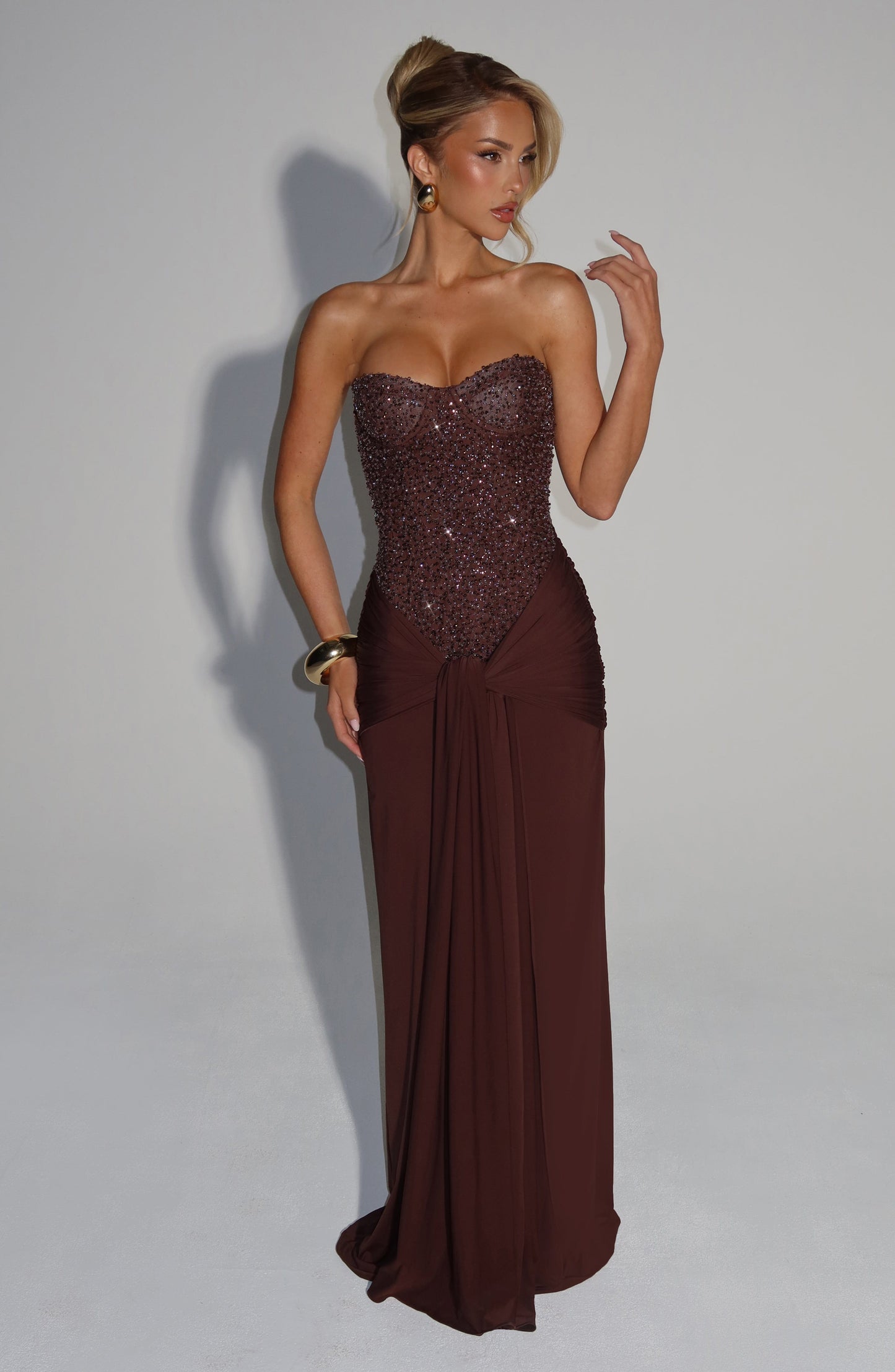 Side view of a women's elegant strapless formal maxi dress in dark brown, showing the embellished bodice and flowing skirt.