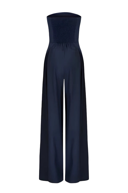Back view of a dark navy strapless wide-leg jumpsuit for women, featuring a smocked back detail on the bodice and a high waist, on a white background.