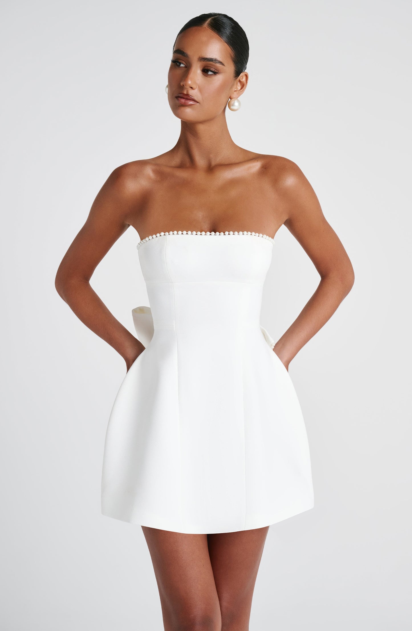 Frontal view of the white strapless mini dress, highlighting the pearl embellished neckline and side pockets.