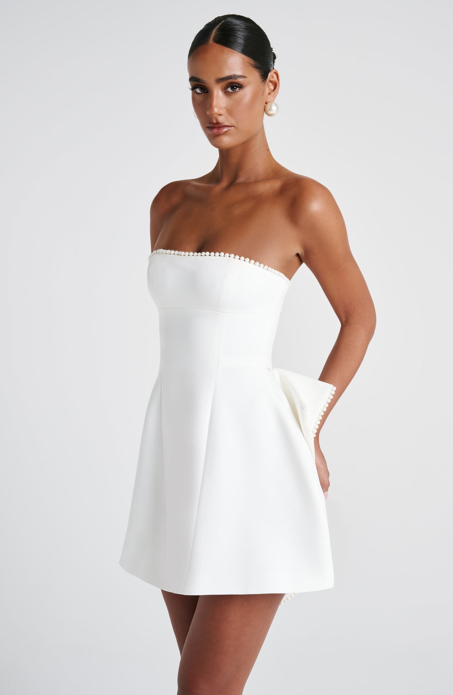 Angled view of the white strapless mini dress, showing the pearl trim and the elegant drape of the fabric.