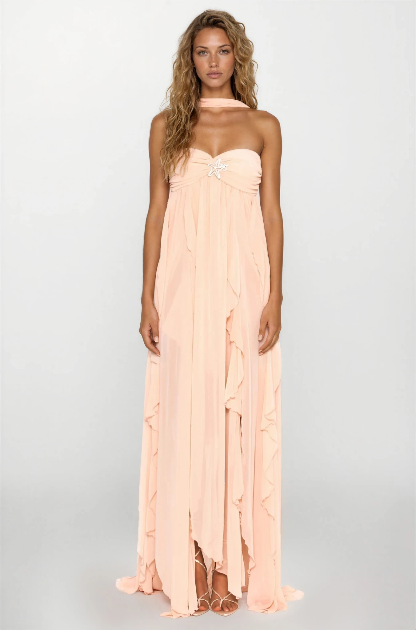 Full view of a model wearing a peach strapless ruched ruffle maxi dress with a star detail and a matching choker.