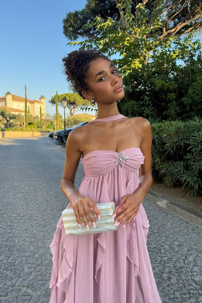 Light pink strapless ruched ruffle maxi dress with a starfish brooch and a matching choker detail, holding an iridescent clutch.