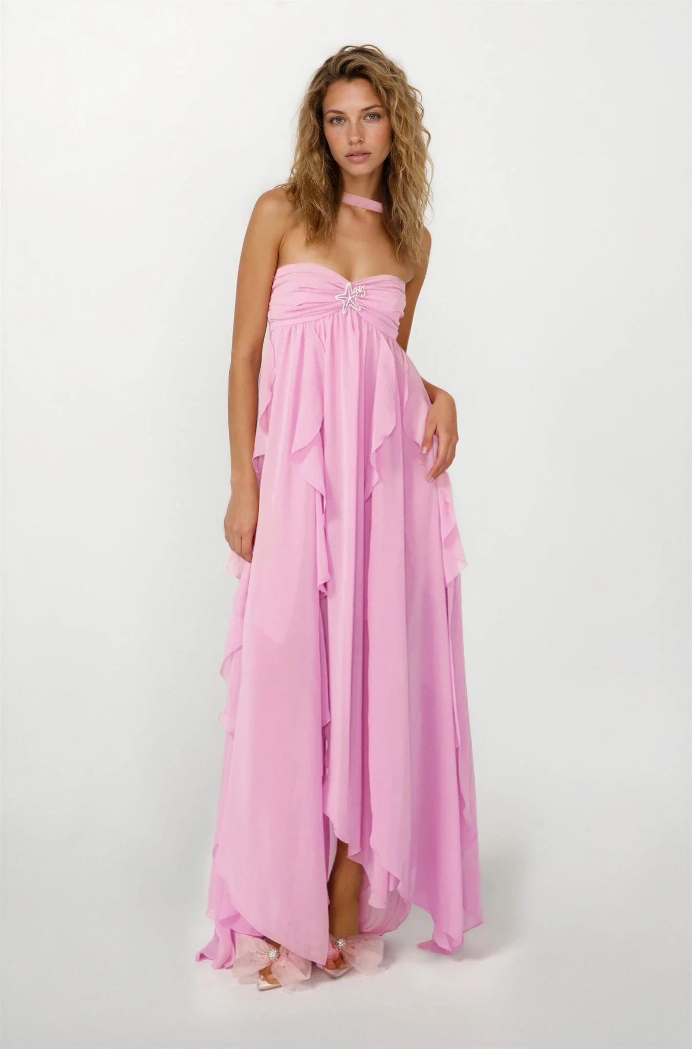 Front view of a women's pink strapless ruched ruffle maxi dress with a starfish brooch and a high-low hem, on a white background.