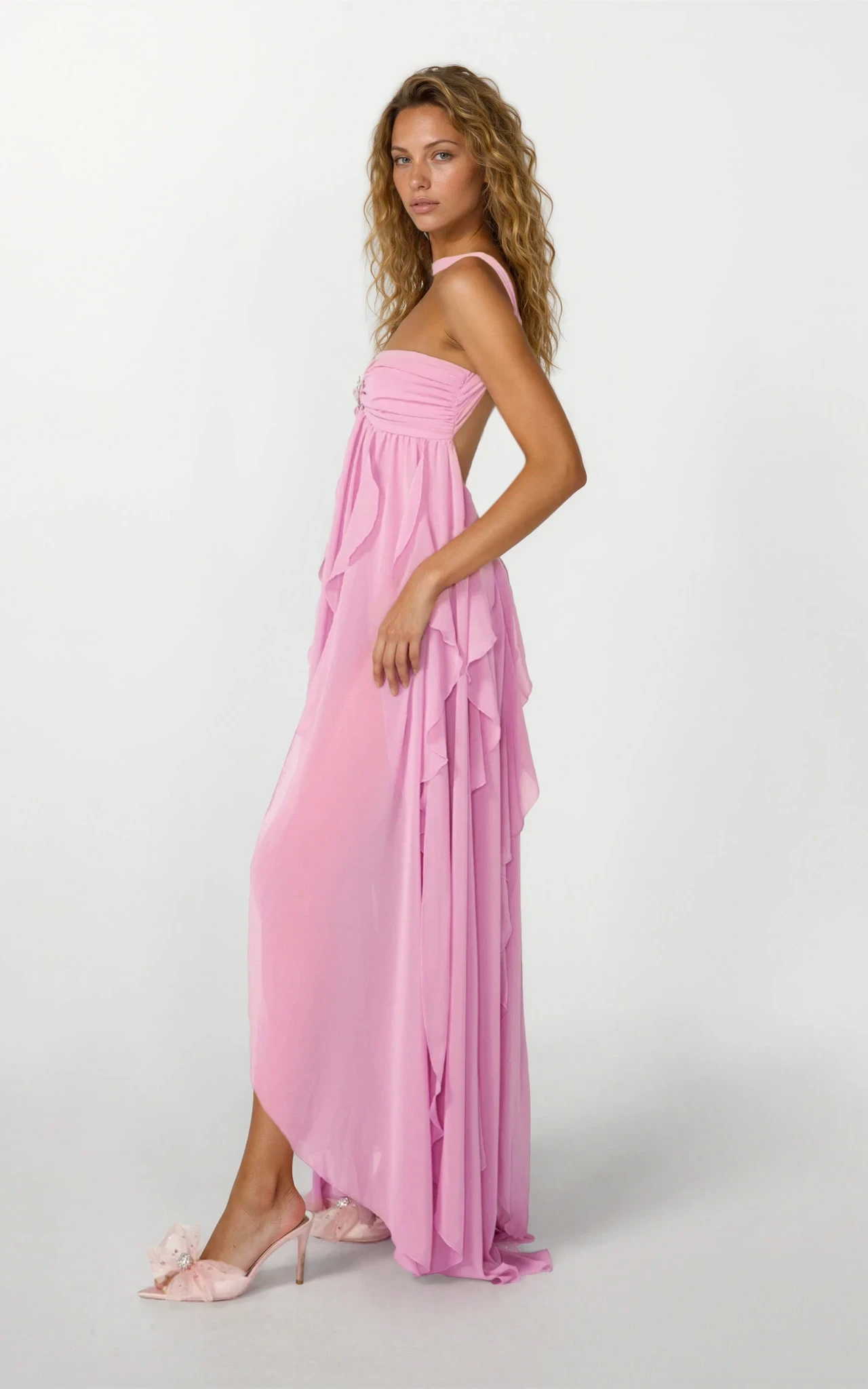 Side view of a women's pink strapless ruched ruffle maxi dress with a starfish brooch and a high-low ruffled skirt.
