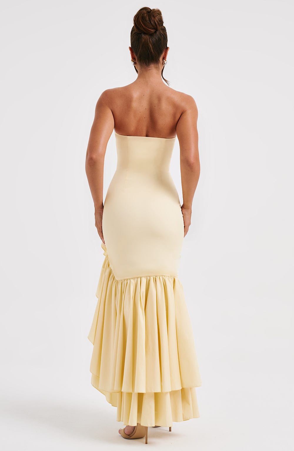 Back view of a women's strapless ruffle high-low maxi dress in light yellow, highlighting the tiered ruffles on the skirt and fitted silhouette.