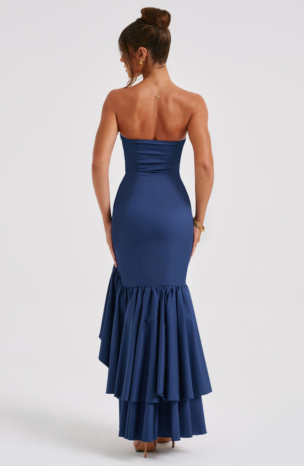 Back view of a women's strapless ruffle high-low maxi dress in navy blue, showing the smooth back and layered ruffles of the skirt.