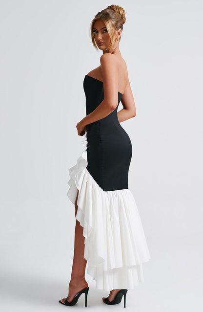 Profile view of a black and white strapless ruffle high-low maxi dress, highlighting the white ruffled train.