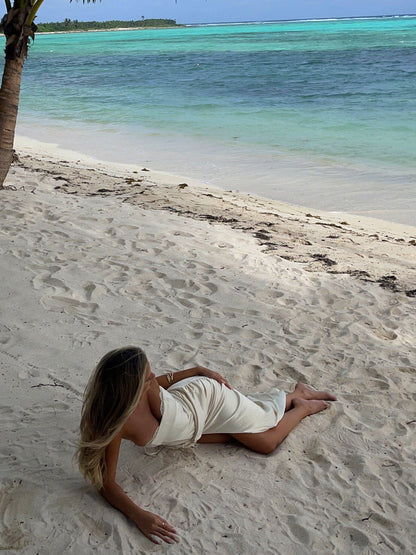 Women's white satin maxi dress with a relaxed fit, lying on a sandy beach with ocean in background.