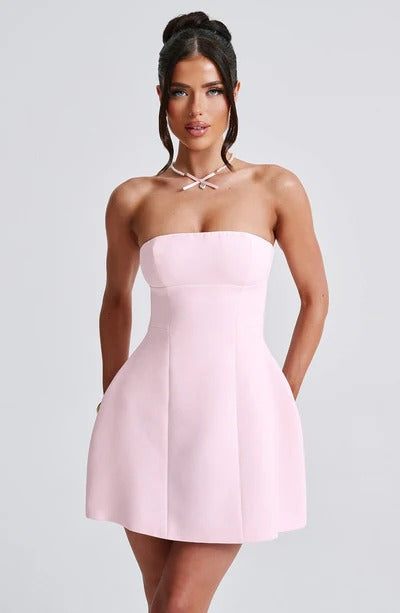 Front view of a woman wearing a light pink strapless seamed bubble mini dress, accessorized with a delicate pearl necklace.
