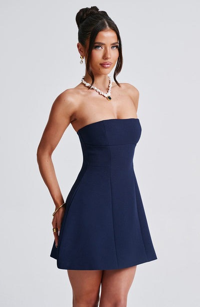 Front view of a navy blue strapless seamed bubble mini dress with a fitted bodice and flared skirt, worn by a model with a pearl necklace.