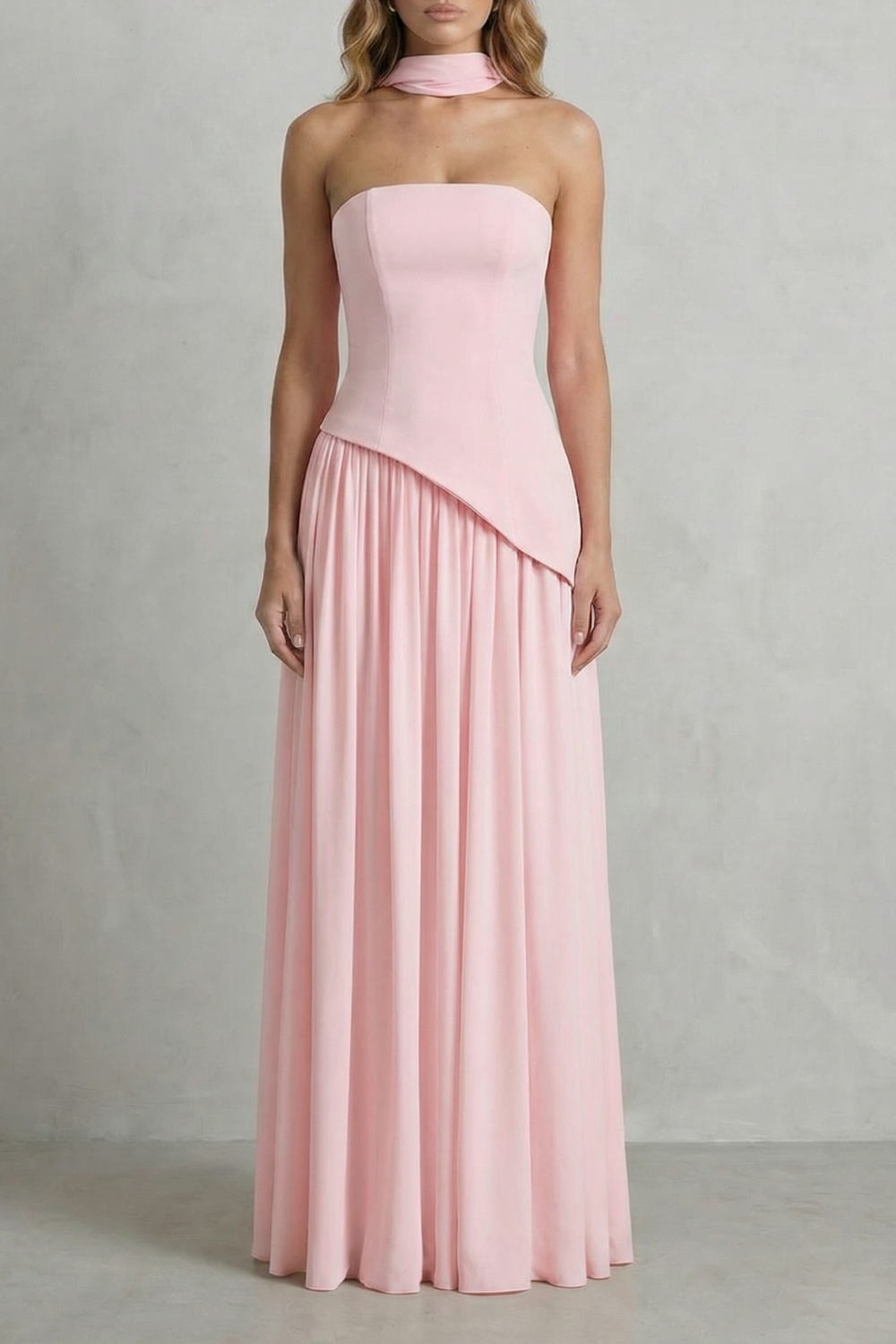 Full-length light pink strapless maxi dress with draped neck detail and asymmetric bodice, suitable for elegant events or as a vacation dress.