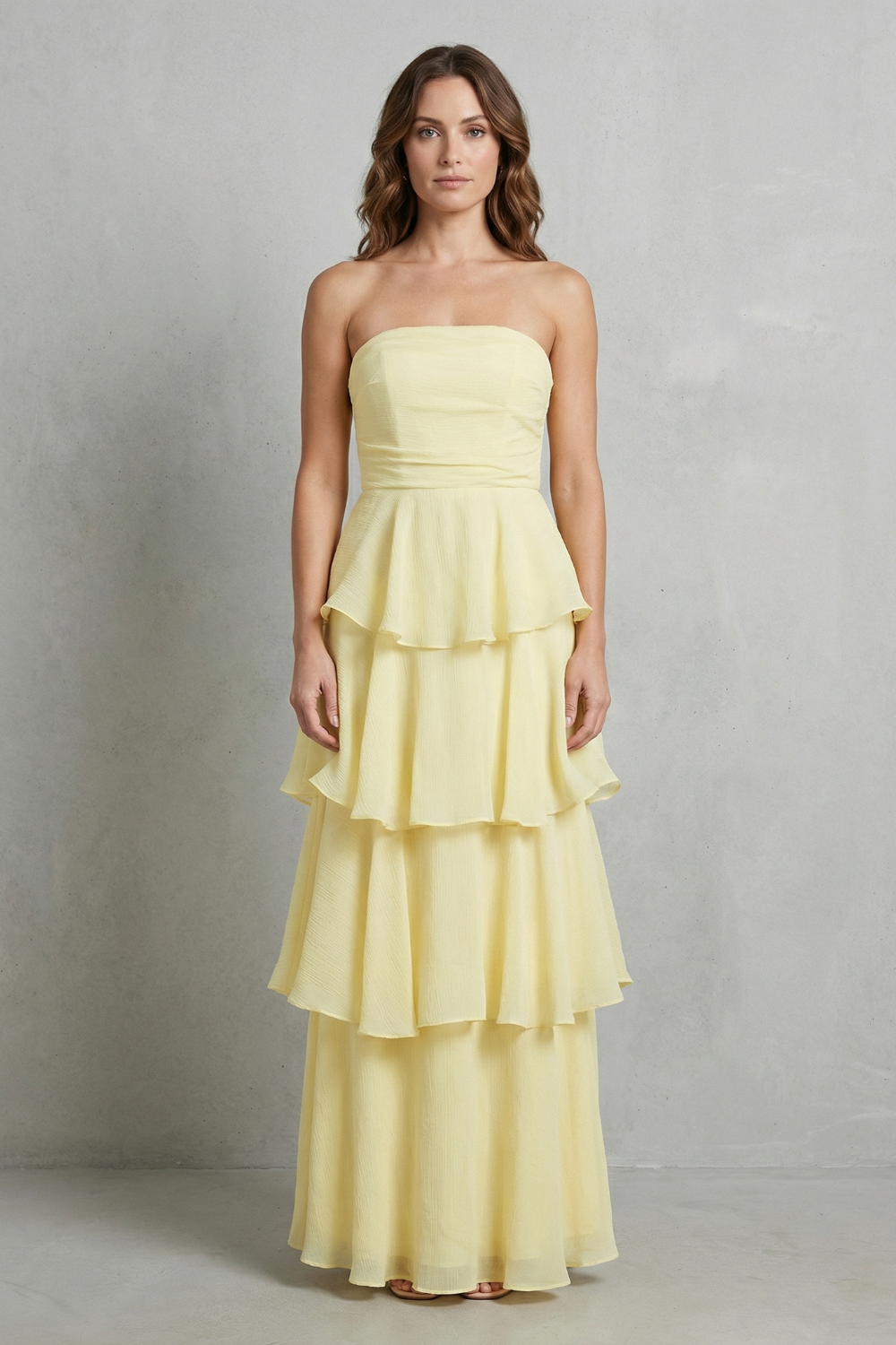 Front view of a woman wearing a pale yellow strapless tiered ruffle maxi dress, ideal for vacation outfits.