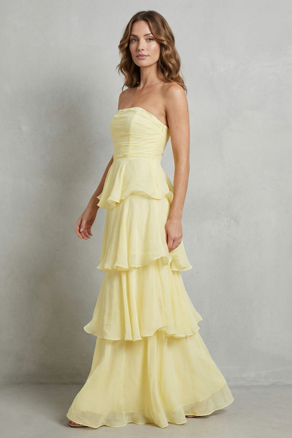Side profile of a woman in a light yellow strapless tiered ruffle maxi dress, showing flowy fabric.