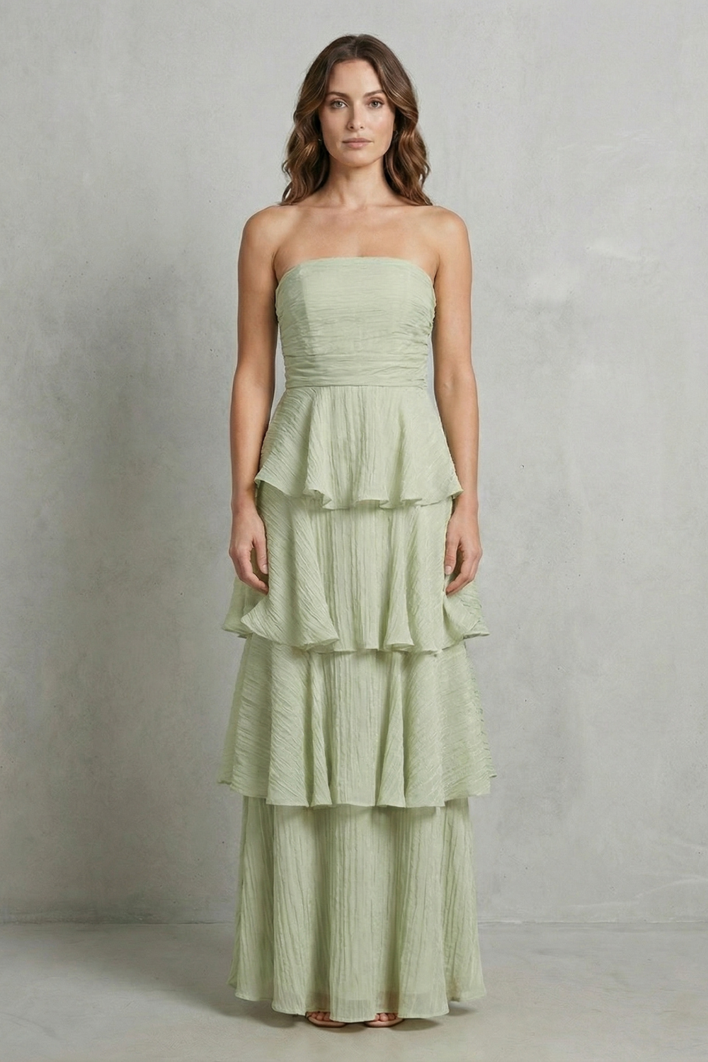 Front view of a woman wearing a sage green strapless tiered ruffle maxi dress, with soft ruffles.