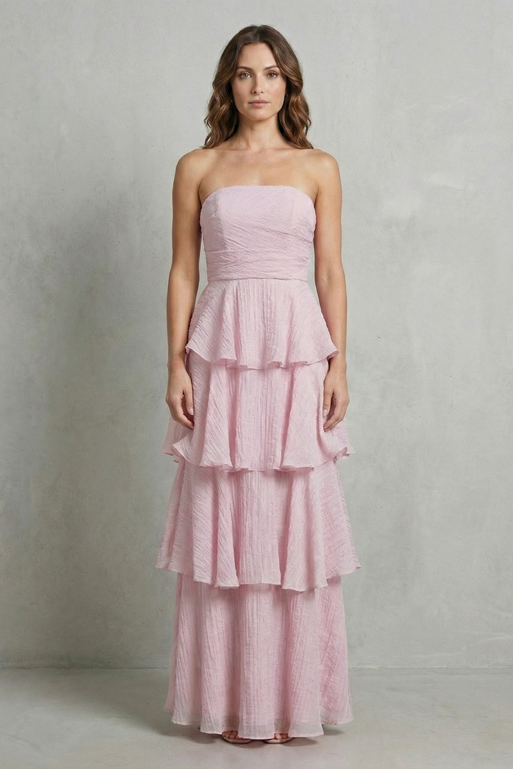 Elegant light pink strapless tiered ruffle maxi dress with a fitted bodice and flowing skirt, ideal as a wedding guest dress.