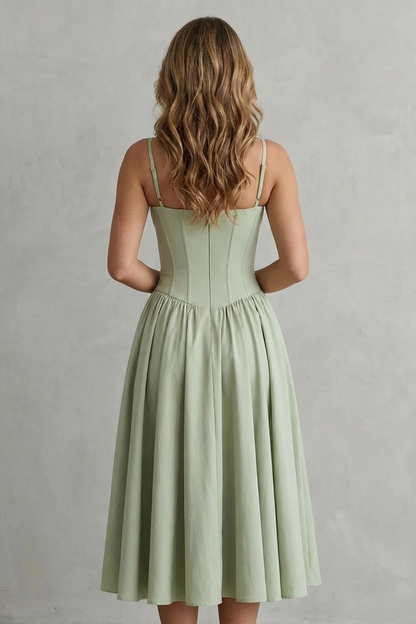 Back view of a woman in a light sage green strappy structured sweetheart neck midi dress, highlighting the corset-style back and pleated skirt.