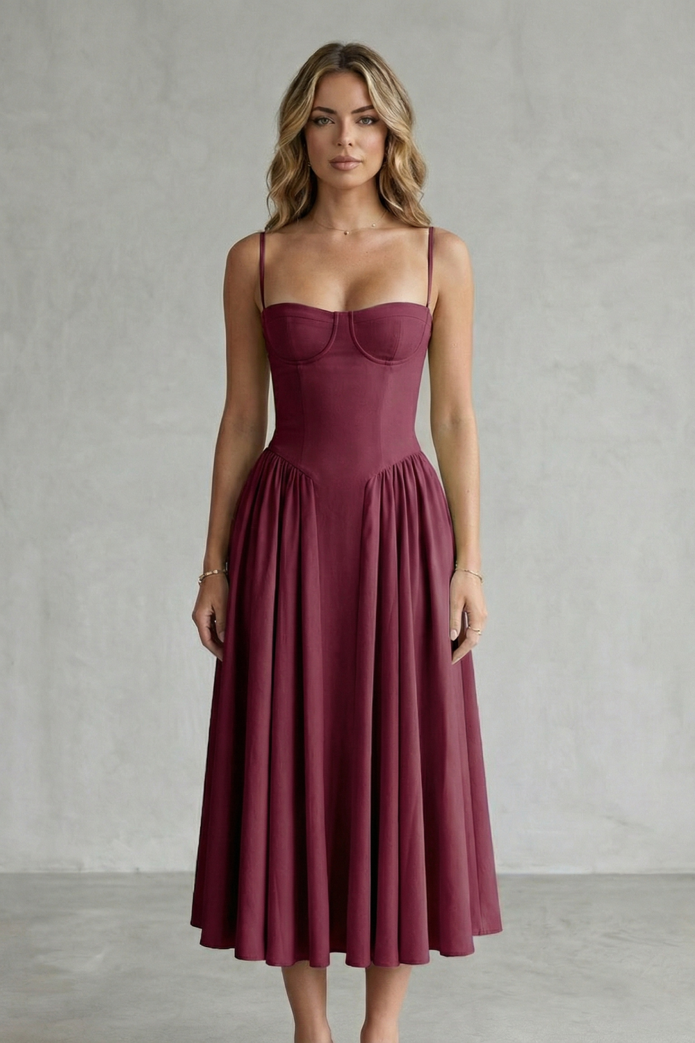 Front view of a woman wearing a deep burgundy strappy structured sweetheart neck midi dress with a full pleated skirt, elegant for wedding guests.