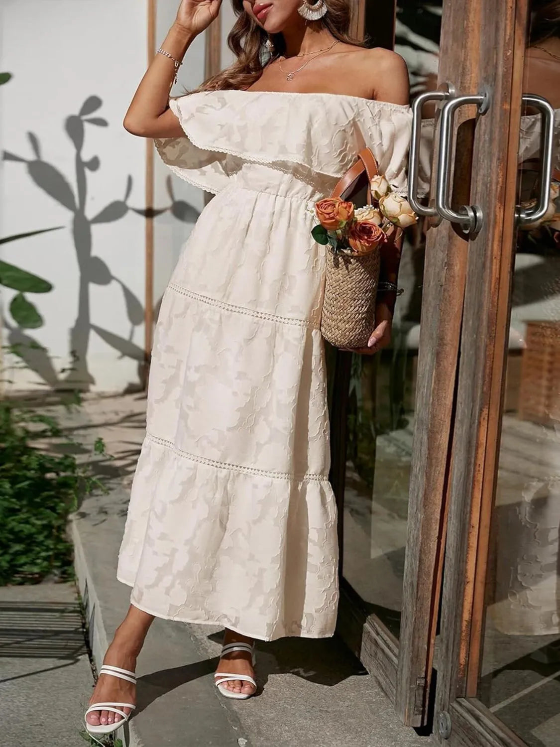 Full-length view of a cream off-shoulder tiered maxi dress with a textured floral design, elastic waist, and flowy skirt.