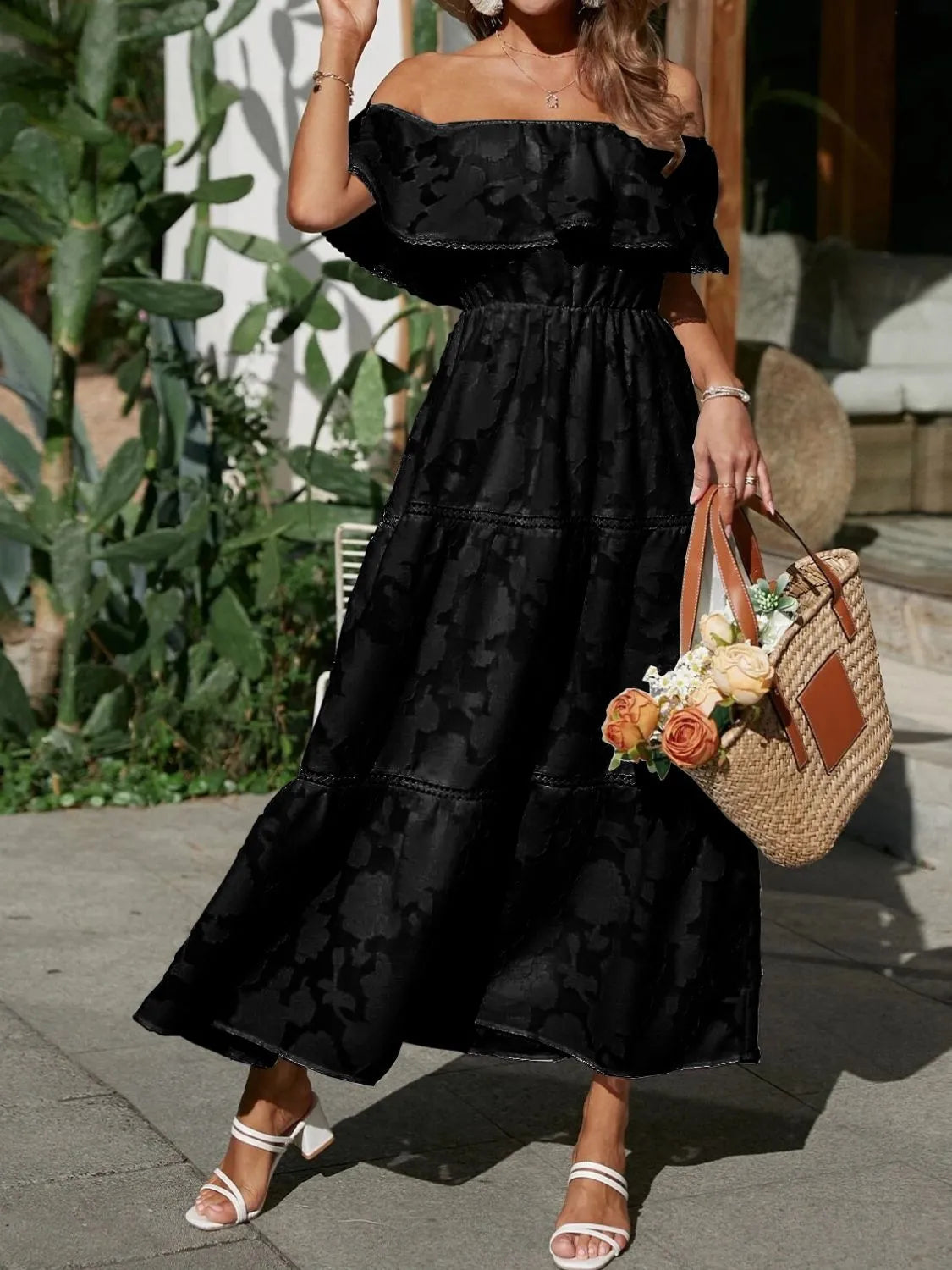 Front view of a black off-shoulder tiered maxi dress for women, featuring a subtle floral texture and ruffled neckline. Elegant dress.